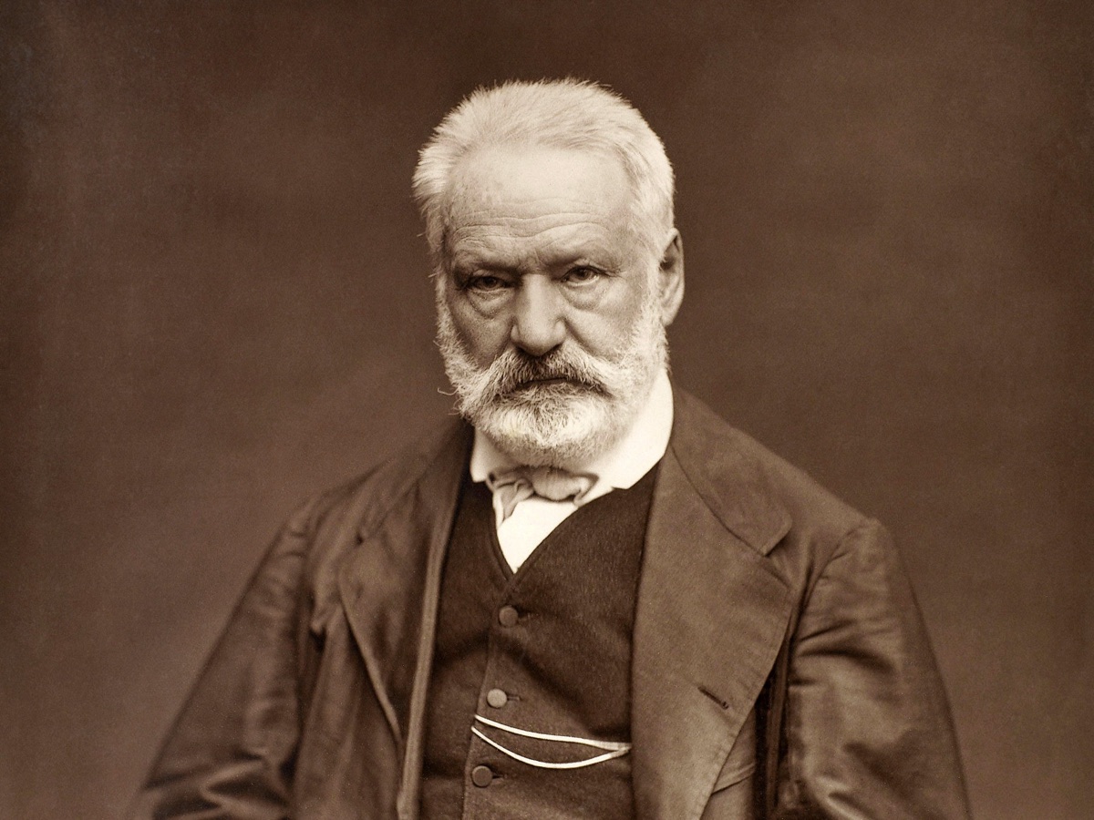 Old photograph of Victor Hugo with white hair and a white beard, in a dark suit